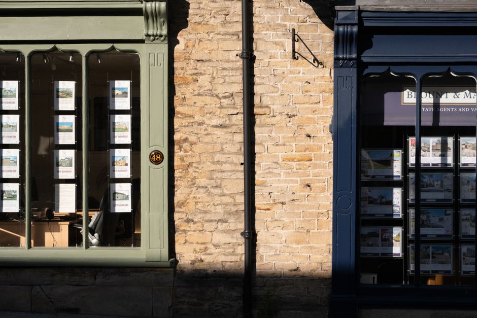 Traditional estate agent shopfront window in a Cotswold stone building, displaying property listings